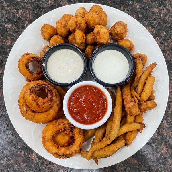 A white plate with fried mushrooms, onion rings, and zucchini fries, served with three dipping sauces.
