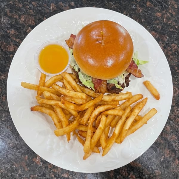 Bacon cheeseburger with lettuce and a side of golden french fries and dipping sauce on a white plate.