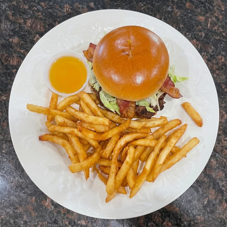 Bacon cheeseburger with lettuce and a side of golden french fries and dipping sauce on a white plate.