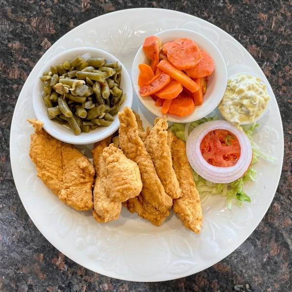 Fried chicken tenders with green beans, carrots, tartar sauce, and a tomato and onion salad.