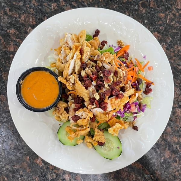 Crispy chicken salad with mixed greens, cranberries, walnuts, and a side of orange dressing.