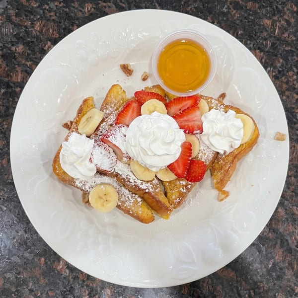 French toast topped with strawberries, bananas, whipped cream, powdered sugar, and a side of syrup.